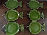 six green fish shaped dishes sitting on a wooden table