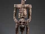 une statue représentant un squelette portant un crâne humain sur le dos