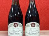 two bottles of red wine sitting on top of a wooden table