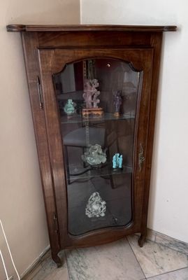 une armoire d'angle avec une porte vitrée, placée dans un coin de la pièce