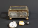 une boîte en argent avec un couvercle en verre et une montre de poche en argent posée à côté