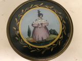 une petite boîte noire et dorée sur laquelle figure l'image d'une femme en robe rose
