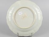 underside view of a white plate with a gold rim on a metal stand