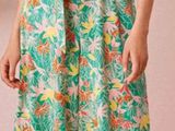 une femme debout devant une plante, vêtue d'une combinaison verte à motifs floraux