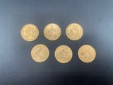 six gold sovereigns are arranged in a row on a black surface
