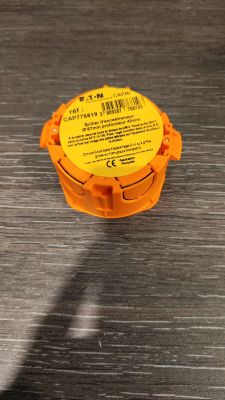 un récipient en plastique orange muni d'une étiquette jaune, posé sur une surface métallique