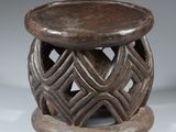 un vieux tabouret en bois dont l'assise est ornée d'un motif sculpté