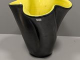 yellow and black vase on a white table with a gray background