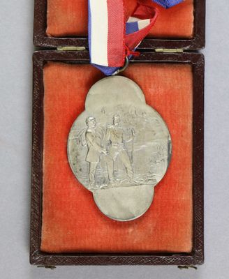 une vieille médaille en argent dans un écrin en velours rouge, entourée d'un ruban