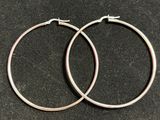 une paire de boucles d'oreilles créoles en argent posées sur une surface noire
