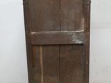 une vieille armoire en bois posée à même le sol, près d'un mur blanc