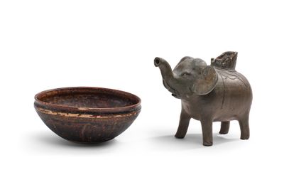 une statue d'éléphant à côté d'un bol, posée sur une surface blanche