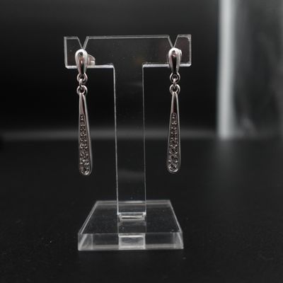 Les boucles d'oreilles sont présentées sur un présentoir transparent posé sur un socle noir