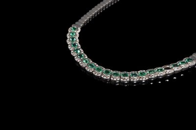 un gros plan d'un collier de diamants et d'émeraudes sur fond noir