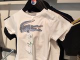 a white t - shirt with a crocodile on it hanging on a rack