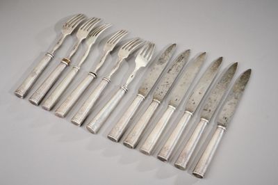 six couverts (fourchettes et couteaux) en métal argenté posés sur un fond blanc
