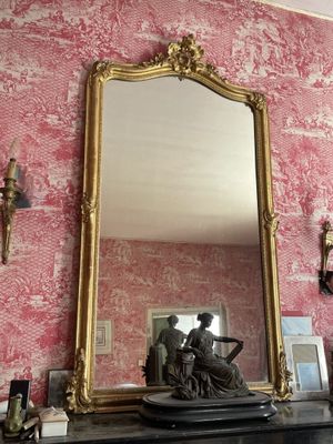 un miroir posé sur une cheminée dans une pièce au papier peint rose