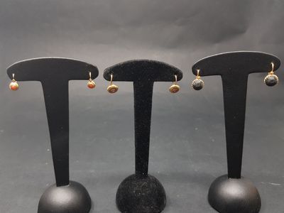 trois paires de boucles d'oreilles posées sur un présentoir noir, sur fond gris