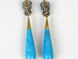 une paire de boucles d'oreilles turquoise et dorées posées sur un fond blanc