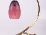 brass table lamp with a pink glass shade on a curved metal stand