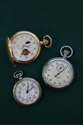 trois types différents de montres de poche posées sur un fond vert