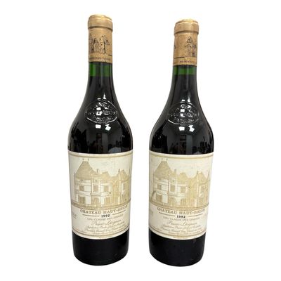 two bottles of red wine sitting next to each other on a white surface