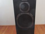 Une enceinte noire est posée sur un parquet, devant un mur blanc.