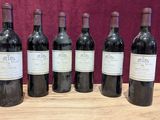 six bottles of red wine are lined up on a wooden table