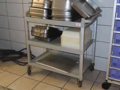 Plusieurs casseroles et poêles sont empilées sur un chariot métallique dans une cuisine.