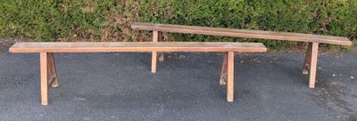 two wooden benches sitting on the pavement near a hedge