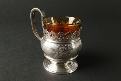 une coupe ancienne en argent, munie d'une anse et d'une poignée, sur un fond noir