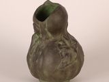 un vase vert orné d'un visage, posé sur un fond blanc