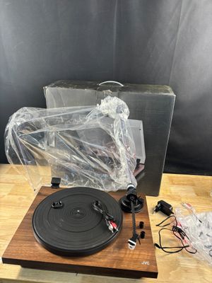 Le tourne-disque est posé sur une table en bois, son boîtier étant emballé dans du plastique.