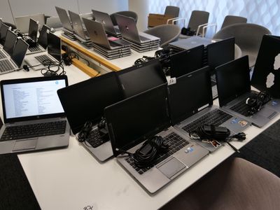 Plusieurs ordinateurs portables sont posés sur une table devant une rangée d'écrans