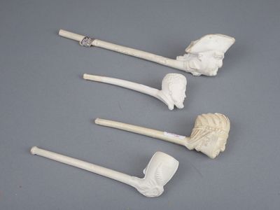 trois porte-pipes blancs ornés de têtes sculptées, posés sur une surface grise