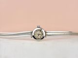 une montre en argent montée sur un bracelet en argent, sur fond rose