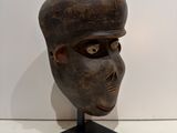 a close up of a wooden mask on a stand on a white surface