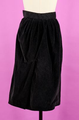 une jupe noire posée sur un mannequin, devant un fond rose