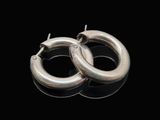 une paire de boucles d'oreilles créoles en argent posées sur un fond noir