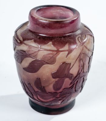un vase violet orné de feuilles, posé sur une surface blanche
