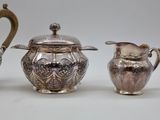 two silver teapots and a creamer on a white surface
