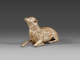 une figurine dorée représentant un mouton sur fond gris