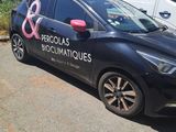 a black car with a pink ribbon on it parked in front of a white van