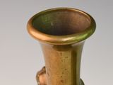 a bronze vase with a bird on it on a white surface