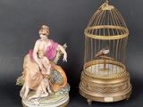 two figurines of a woman and a bird in a cage