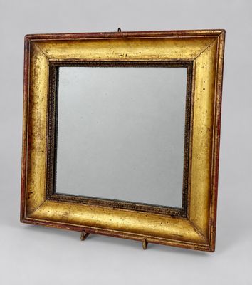 a gold framed mirror with a wooden stand on a grey background