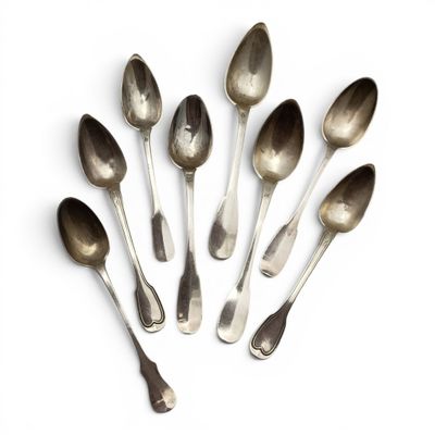 six cuillères en argent sont disposées en cercle sur une surface blanche