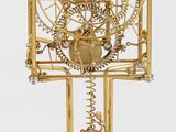 golden clock with gears and wheels on a stand on a white surface