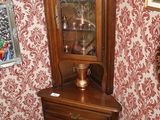 une armoire d'angle avec une porte vitrée, placée dans un coin de la pièce