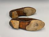 une paire de chaussures en cuir marron posées sur une surface blanche